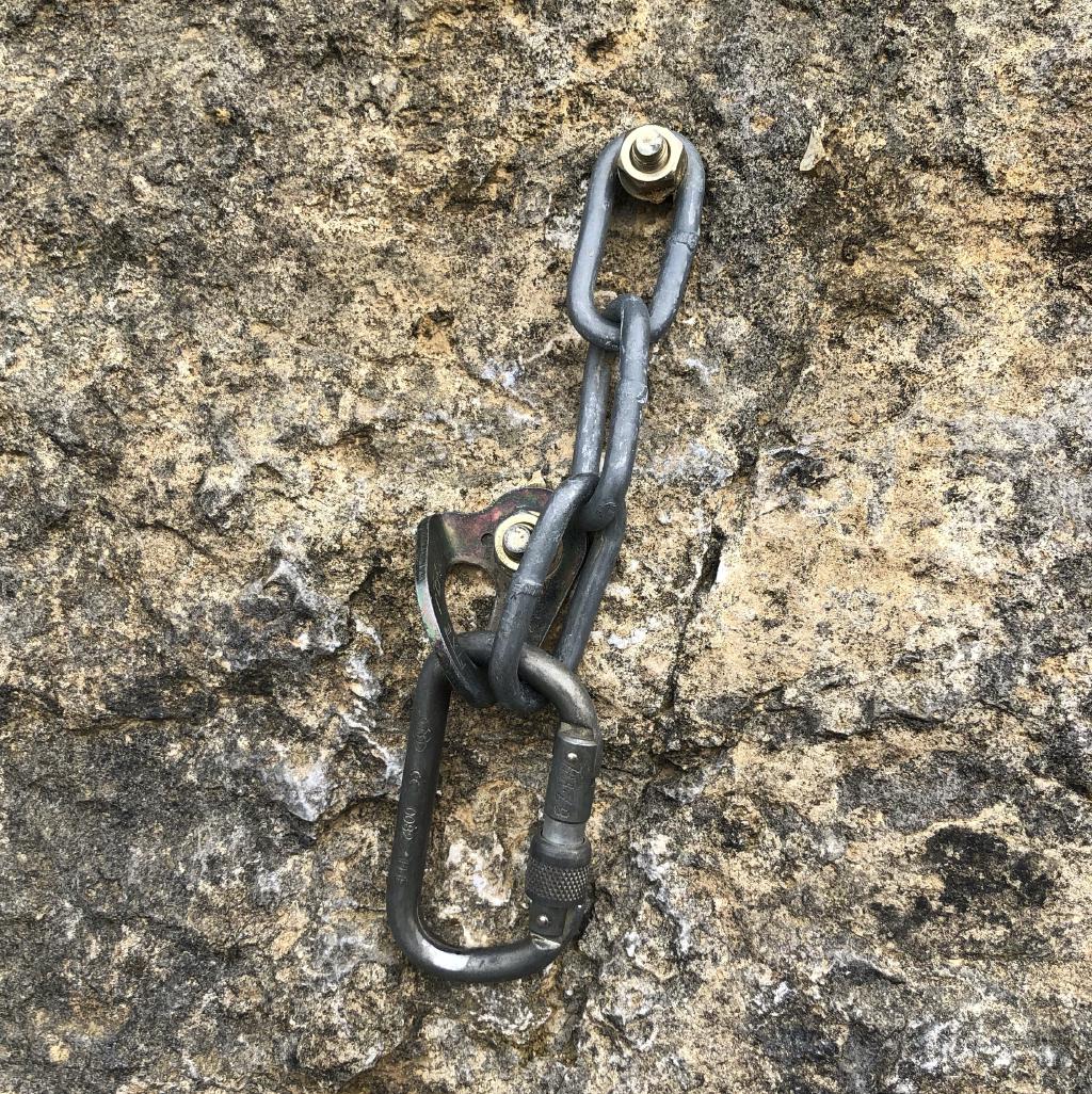 A steel screwgate hanging on a chain and a hanger. The chain has 3 long links and is attached directly to a bolt.