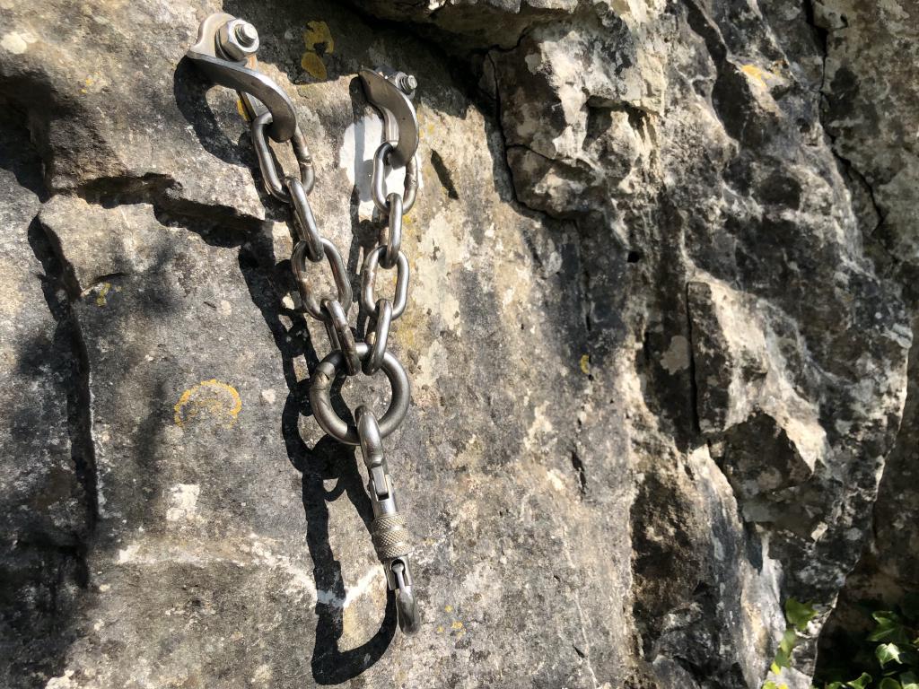 A shiny screwgate carabiner connected by chains to two bolted hangers.