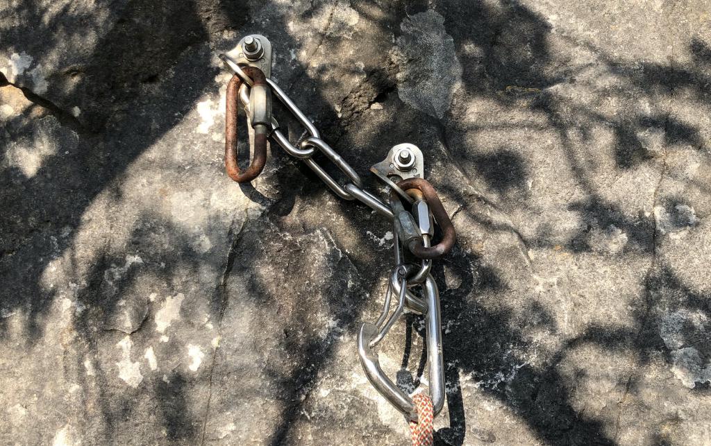 A shiny snapgate attached by chains to two bolts. Each bolt also has an old rusty maillon above the chain.