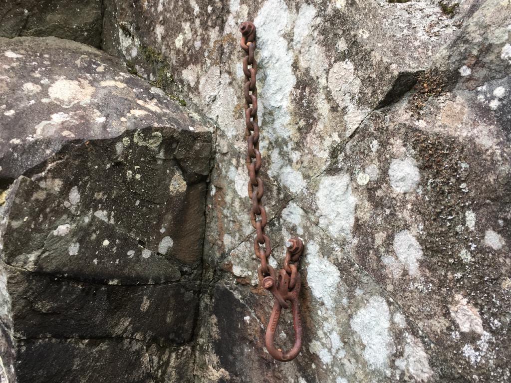 A very rusty, large ring connected to the rock by a short, rusty chain, and a longer, rusty chain to the left.